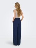 Model draagt donkerblauwe wijde broek met beige top.