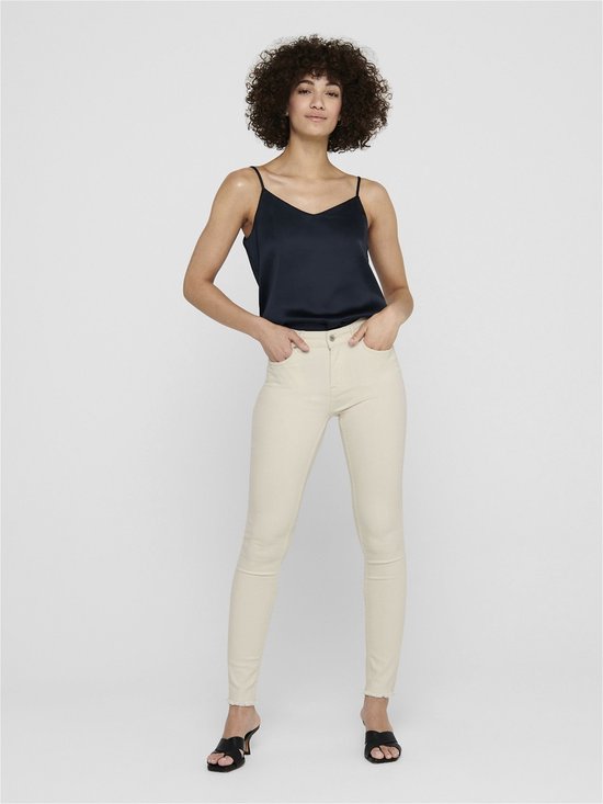Model met een donkerblauwe top en crèmekleurige skinny jeans met rafelige zoom.