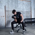 Jonge man met zwart t-shirt en trainingsbroek doet biceps curls met een dumbbell.