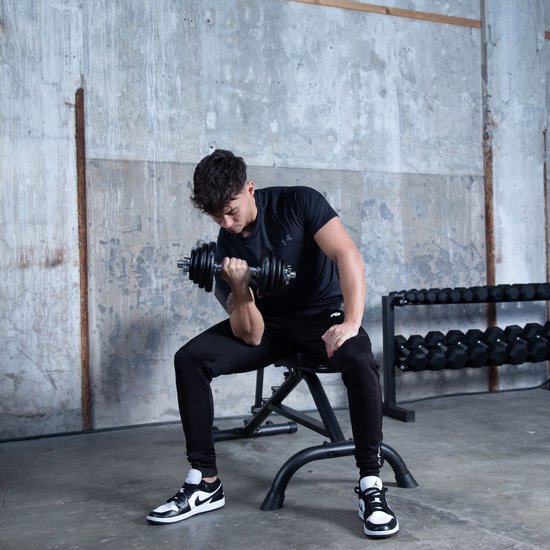 Jonge man met zwart t-shirt en trainingsbroek doet biceps curls met een dumbbell.