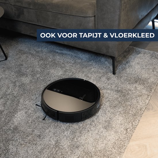 Zwarte robotstofzuiger op dik grijs vloerkleed naast grijze bank.