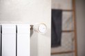 Een witte Netatmo slimme radiatorthermostaat met oranje ring, gemonteerd op een witte radiator.