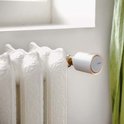 Netatmo slimme thermostaatknop, zilverkleurig met oranje accent, op een oude crèmekleurige radiator.