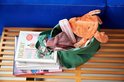 Een lichtbeige Mepal babylepelsset met twee lepels in een houder, liggend in een groene tas naast een stapel tijdschriften en een knuffel.