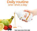 Een hand schenkt MEGA SPORT uit een fles in een maatbeker. Op de achtergrond fruit zoals bananen, een appel, aardbeien, citroen en bosbessen.