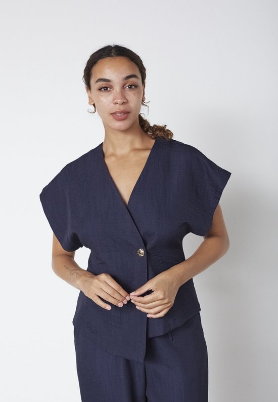 Donkerblauwe top met korte, wijde mouwen en één gouden knoop, gedragen door een model.