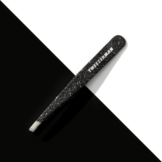 Tweezerman schuin pincet met zwarte glitter, diagonaal geplaatst op een zwart-wit gesplitste achtergrond.