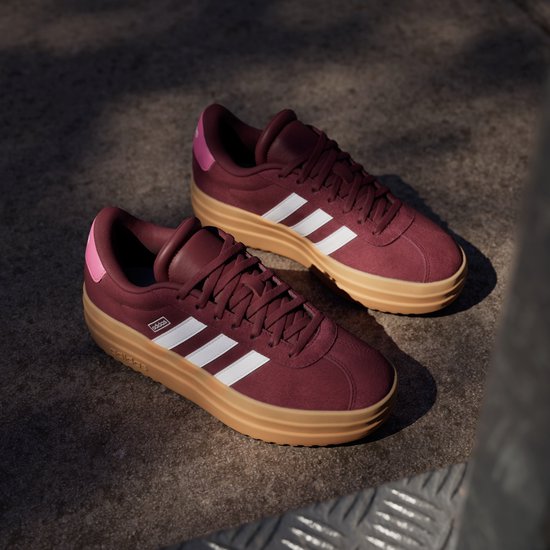 Bordeauxrode Adidas sneakers met witte strepen en bruine zool.