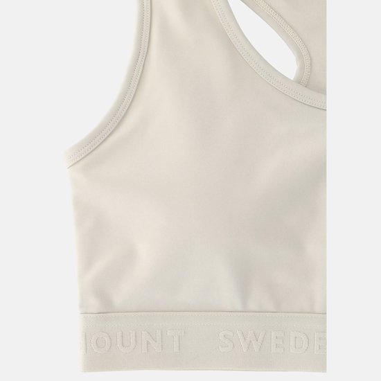 Detail van een lichte sportbeha met racerback. De onderkant heeft een brede band met ingeweven tekst 'SWEDEMOUNT'.