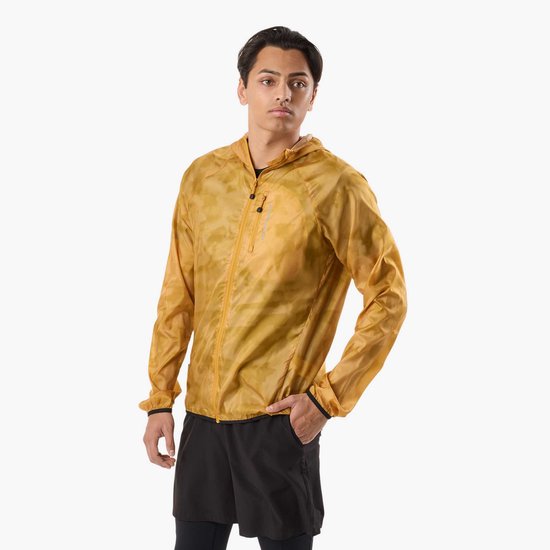 Man in geel, doorschijnend windjack met camouflageprint, hand in zak.