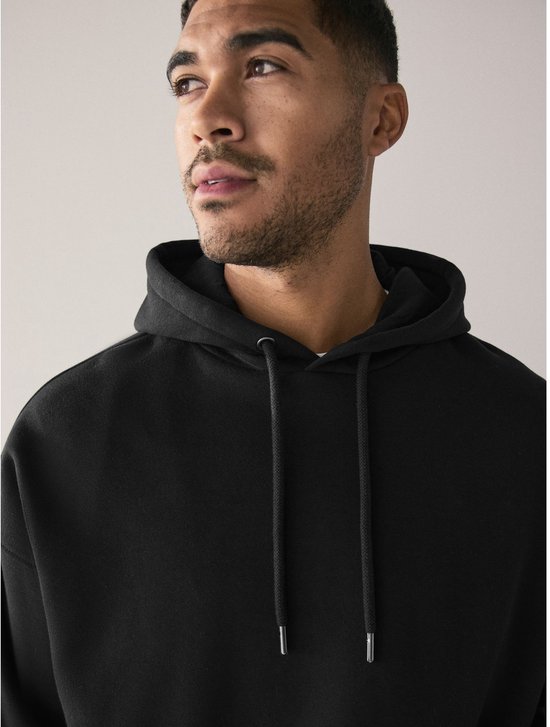 Close-up van een man die een zwarte oversized hoodie met capuchon draagt.