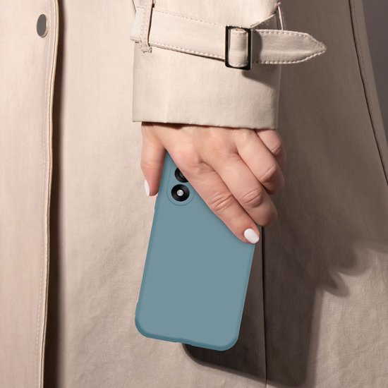 Een hand met witte nagels houdt een matgroen telefoonhoesje vast, met de achterkant naar buiten gericht. Ze draagt een beige trenchcoat.