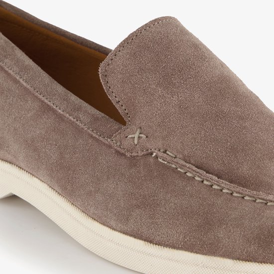 Detail van een bruine suède loafer, met stiksels en de beige zool.