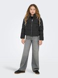 Meisje met lang blond haar in een zwarte pufferjas en wijde grijze jeans.