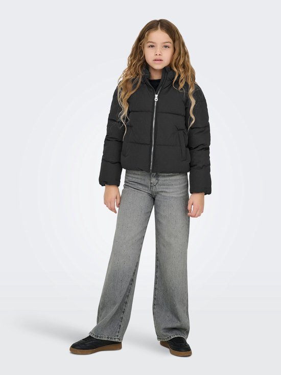 Meisje met lang blond haar in een zwarte pufferjas en wijde grijze jeans.
