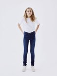Meisje staand in donkerblauwe skinny jeans en een witte top.