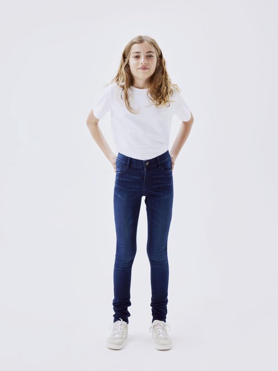 Meisje staand in donkerblauwe skinny jeans en een witte top.