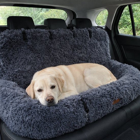Een blonde labrador rust op een donkergrijs, pluizig hondenbed in de achterbank van een auto.