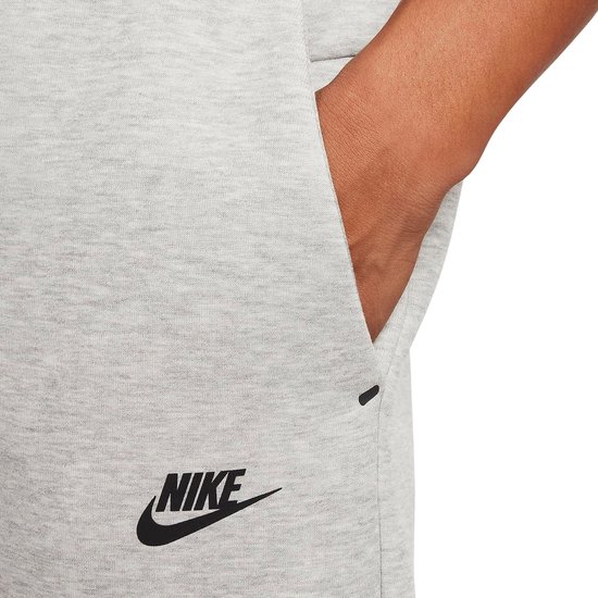Close-up van de grijze Nike joggingbroek met een zwart Nike logo en een klein zwart streepje.