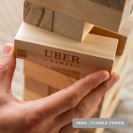 Close-up van hand die een houten blok uit de stapeltoren trekt. 'UBER GAMES' logo zichtbaar.