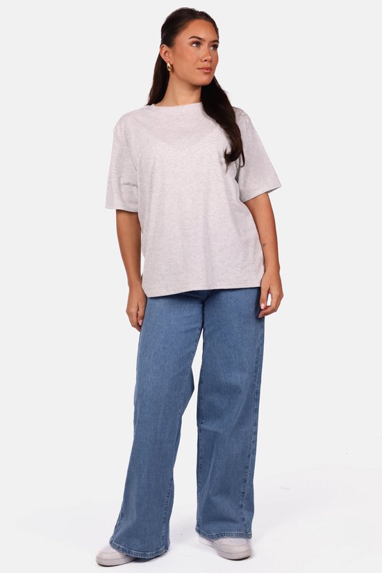 Model in een lichtgrijs, oversized T-shirt en wijde jeans.