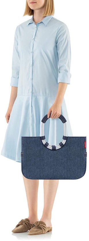 Vrouw draagt donkerblauwe shopper met zilveren hengsels en spijkerstof textuur.