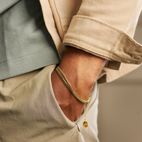 Gouden dubbele schakelarmband gedragen door een man. Muntvormige bedel met 'A ARKAI' erop.