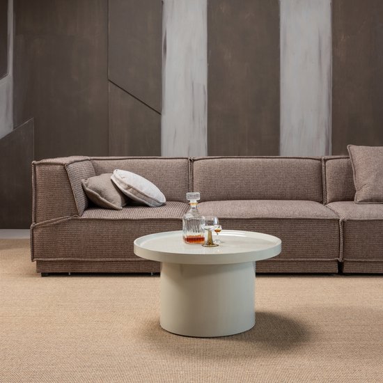 Bruine stoffen hoekbank met een ronde, hoogglans zandkleurige bijzettafel met een karaf en glazen.