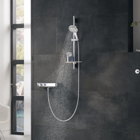 Een chroomkleurige doucheslang met handdouche in een moderne douchecabine met donkere tegels.