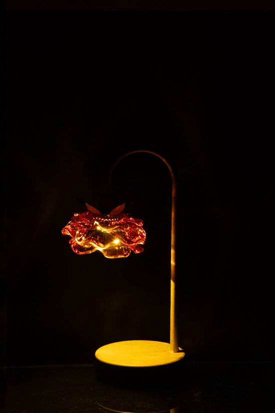 Abat-jour en verre orange en forme de fleur, éclairé, sur un support en fer, sur fond noir.