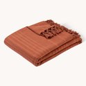 Gevouwen terracotta plaid met franjes, liggend op een witte achtergrond.