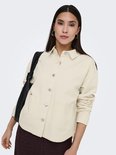 Gebroken witte spijkerjas met lange mouwen, borstzakken en zilverkleurige knopen, gedragen over een donkerbruine broek.