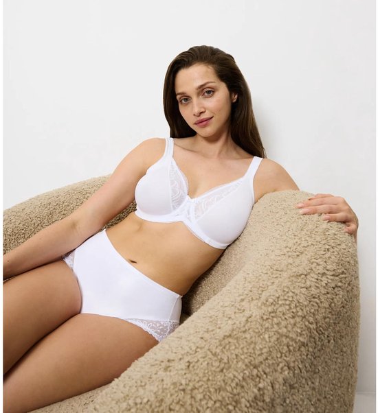 Model zit in een stoel, draagt een witte beha met kanten details en een wit broekje.
