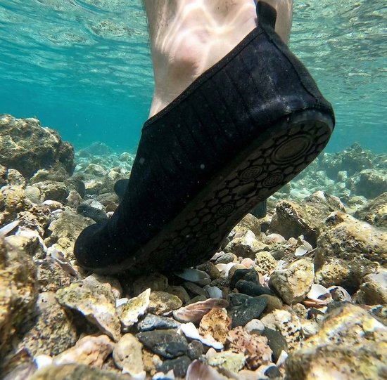 Zwarte waterschoen met antislipzool, gedragen op rotsachtige bodem onder water.
