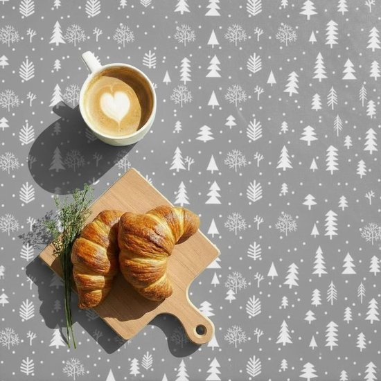 Nappe grise avec motif d'arbres de Noël blancs et une tasse de café avec latte art en forme de cœur.