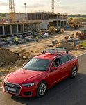 Rode Audi stationwagon op een bouwplaats met kranen en bouwvakkers.