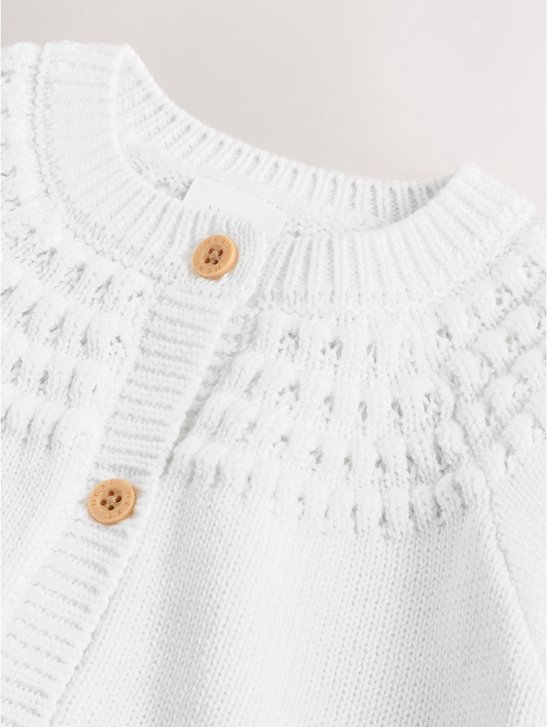 Halslijn van witte babyvest met ajourdetails en houten knopen.