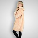 Een vrouw met blond haar draagt een oversized beige hoodie deken. Ze staat met haar rug naar de camera en kijkt over haar schouder naar de kijker.
