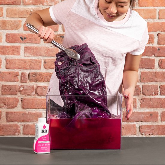 Vrouw kleurt een paarse jeans fuchsia in een bak met kleurstof.