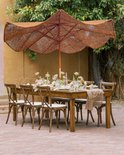 Een bruine parasol met golvende rand boven een gedekte tafel voor een buitenevenement.