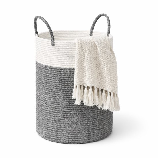 Grijze en witte katoenen wasmand met handgrepen en een gebreide deken met franjes.