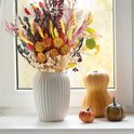 Boeket gedroogde bloemen in herfstkleuren in een witte vaas op een vensterbank, met pompoenen ernaast.