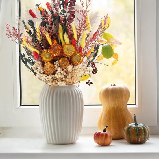 Boeket gedroogde bloemen in herfstkleuren in een witte vaas op een vensterbank, met pompoenen ernaast.