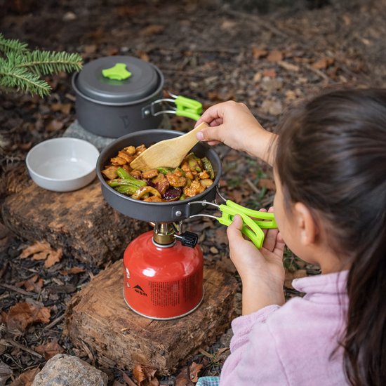 Kind kookt eten in een pannenset op een rood kampeerkooktoestel.