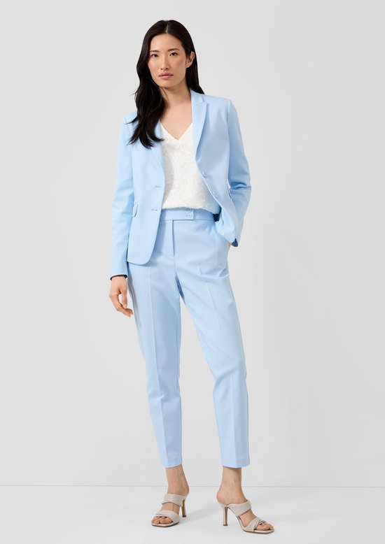 Vrouw in lichtblauwe blazer en broek met witte top, hoge hakken.