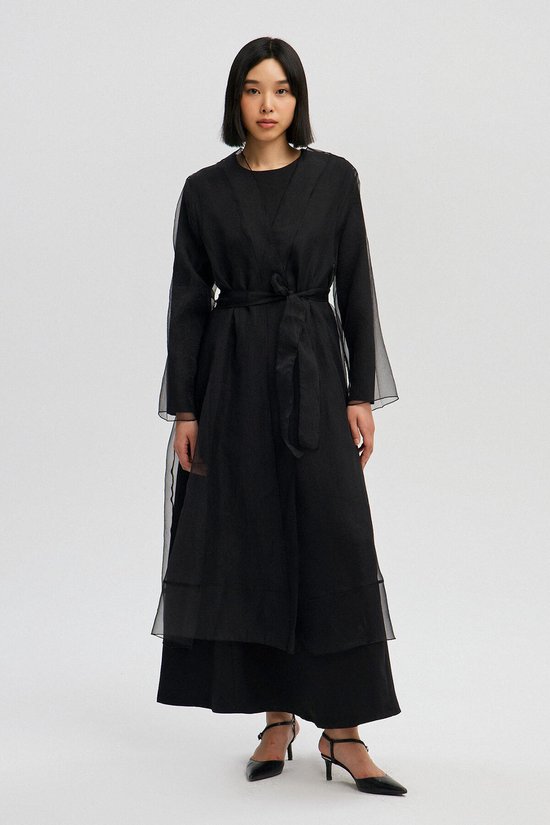 Model van voren, draagt een lange zwarte kimono met ceintuur en doorschijnende mouwen.