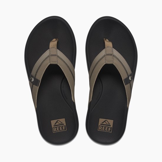 Paar zwarte teenslippers met beige bandjes, Reef logo op de zwarte binnenzool.