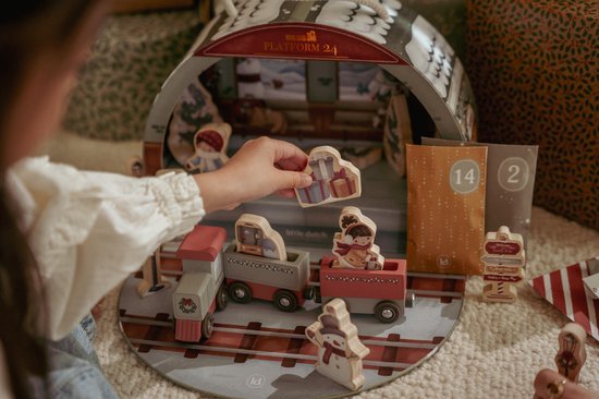 Meisje speelt met een houten trein en kerstfiguurtjes, met adventszakjes op de achtergrond.
