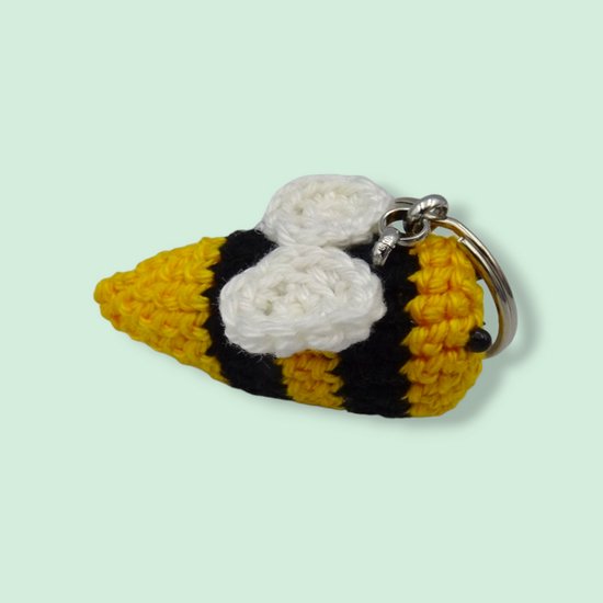 Gehaakte bijensleutelhanger met gele, zwarte en witte strepen, en witte vleugels.
