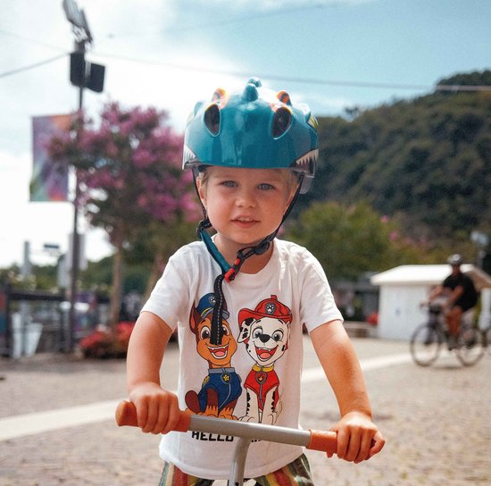 Jongen met blauwe dinosaurushelm en Paw Patrol T-shirt op een loopfiets.